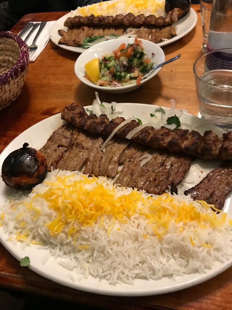 Two plates of rice and kebabs with a side of shirazi salad courses