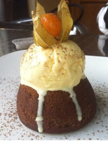 Small chocolate cake topped with a scoop of ice cream and a gooseberry.