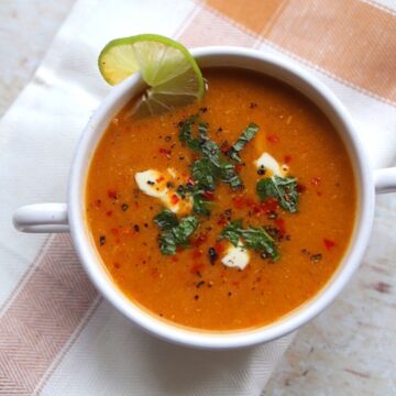 Image of red Turkish lentil soup in a white bowl with fresh herbs and yogurt.