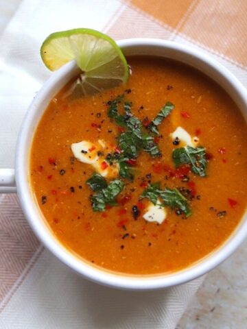 Image of red Turkish lentil soup in a white bowl with fresh herbs and yogurt.