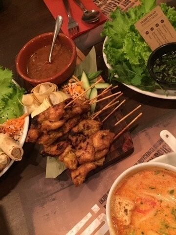 Overhead view of table with soup, spring rolls and chicken satay on skewers.