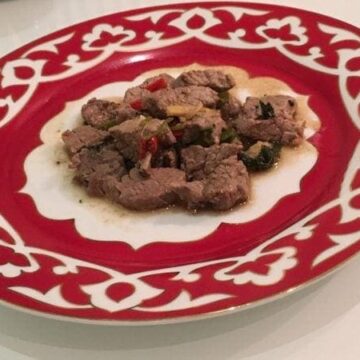 Serving of beef on red and white plate.