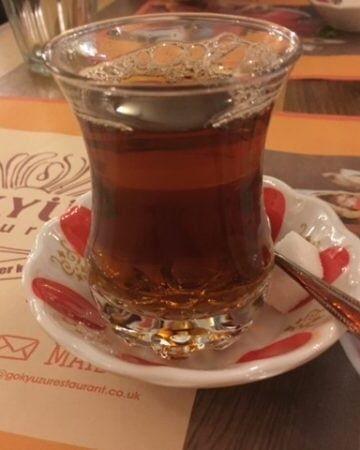 Turkish tea in a small glass on red and white saucer with sugar cube.