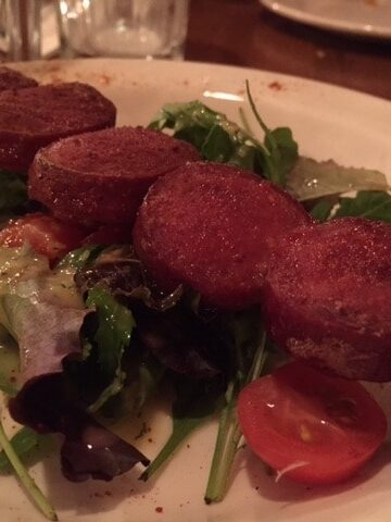 A skewer of sliced sucuk sausage with salad on a white plate.