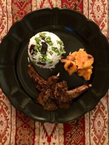 Lamb chops with rice and sweet potato on black plate.