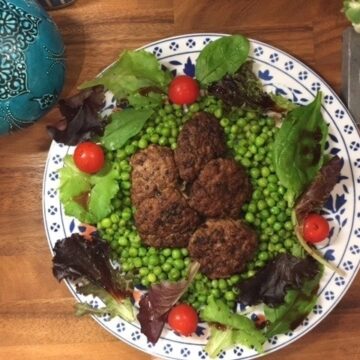Turkish meatballs on bed of peas on a platter surrounded by salad.