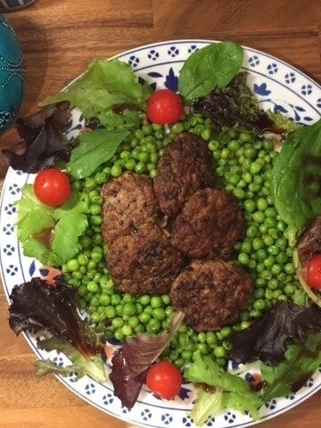 Turkish meatballs on bed of peas on a platter surrounded by salad.