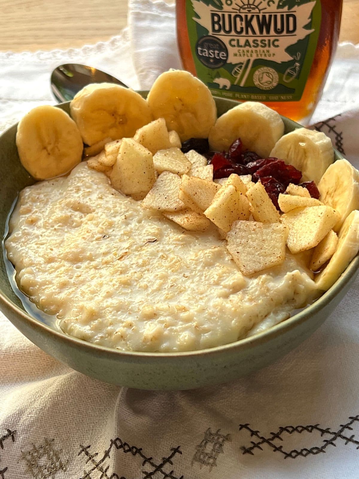 Porridge with fruit garnish in green bowl next to bottle of maple syrup.