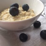 cooked oatmeal with blueberries in small white bowl