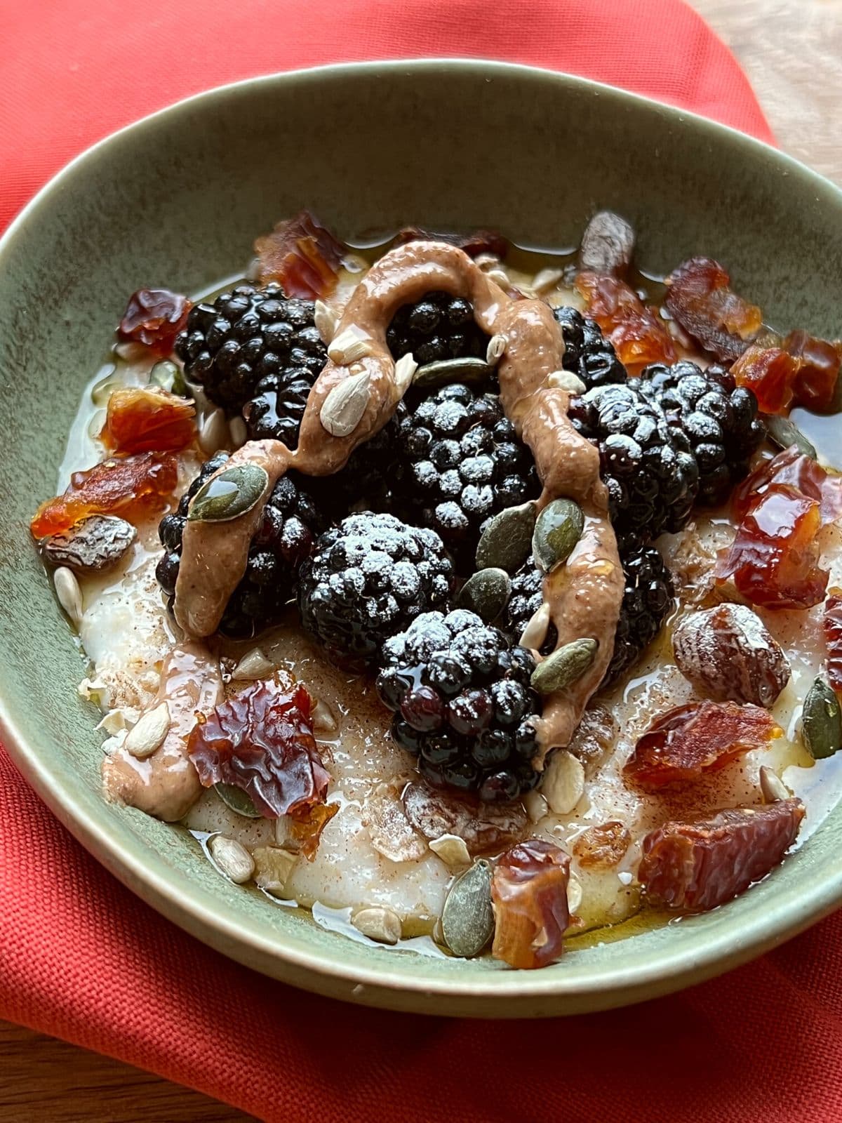 Porridge in green bowl with fruit and nut toppings.