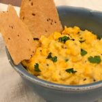 Image of corn dip in a blue bowl with Indian flatbread and cilantro garnish.