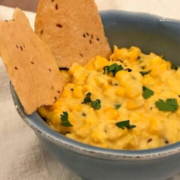 Image of corn dip in a blue bowl with Indian flatbread and cilantro garnish.