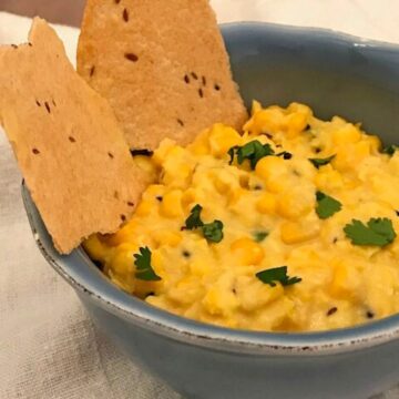 Image of corn dip in a blue bowl with Indian flatbread and cilantro garnish.