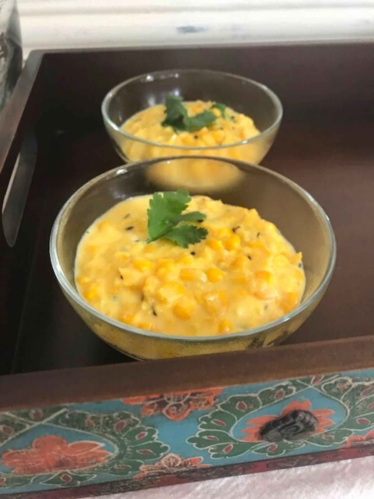 Two bowls of corn on wooden tray