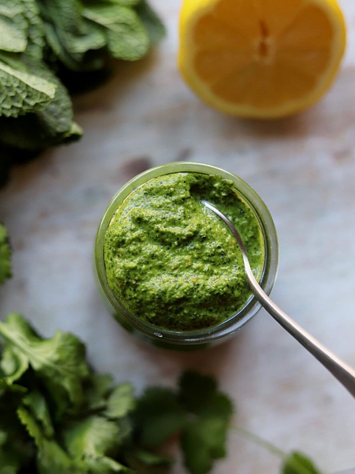 Chutney in glass jar with metal spoon and lemon and herbs.