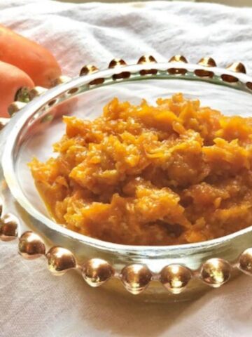 halwa in decorative glass bowl alongside 2 carrots