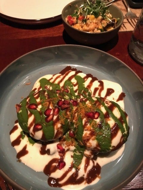 Two Aloo Tikki in yogurt and chutney on a plate and side of quinoa salad