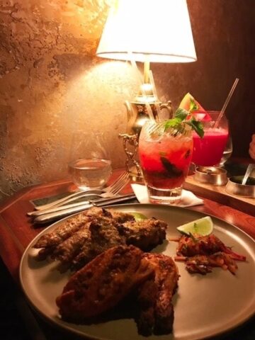 food on plate with red drinks lit by a table lamp