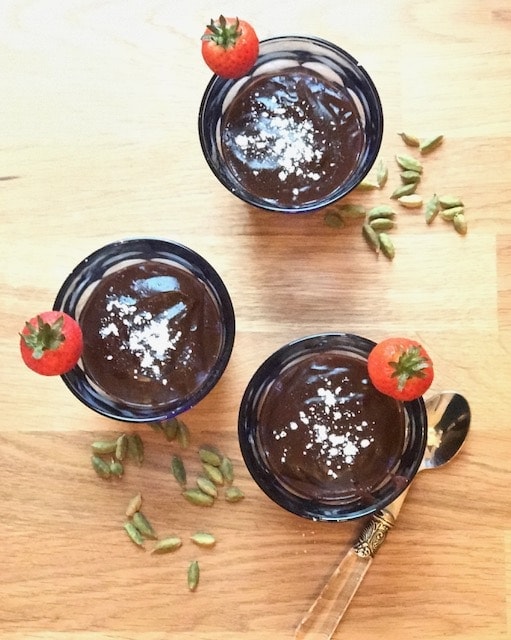 top view of glasses with chocolate pudding and strawberries with scattered cardamom 