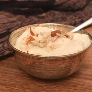 closeup of kheer in small silver bowl garnish with crushed almonds
