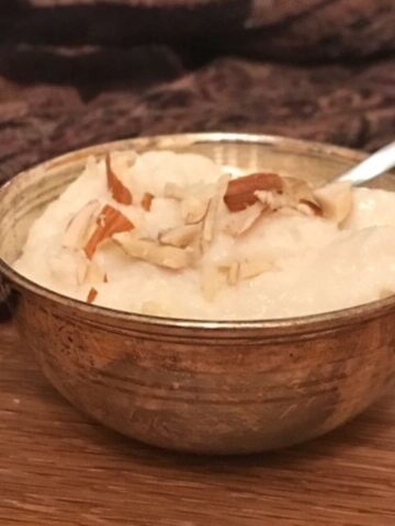 closeup of kheer in small silver bowl garnish with crushed almonds