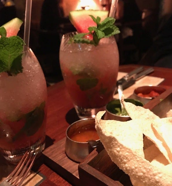 Dining table with poppadums, three dips and watermelon drinks in glasses with crushed ice