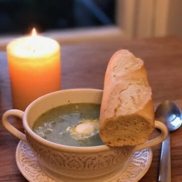 Broccoli soup in white bowl with bread next to a candle
