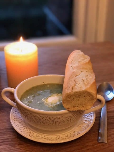 Broccoli soup in white bowl with bread next to a candle