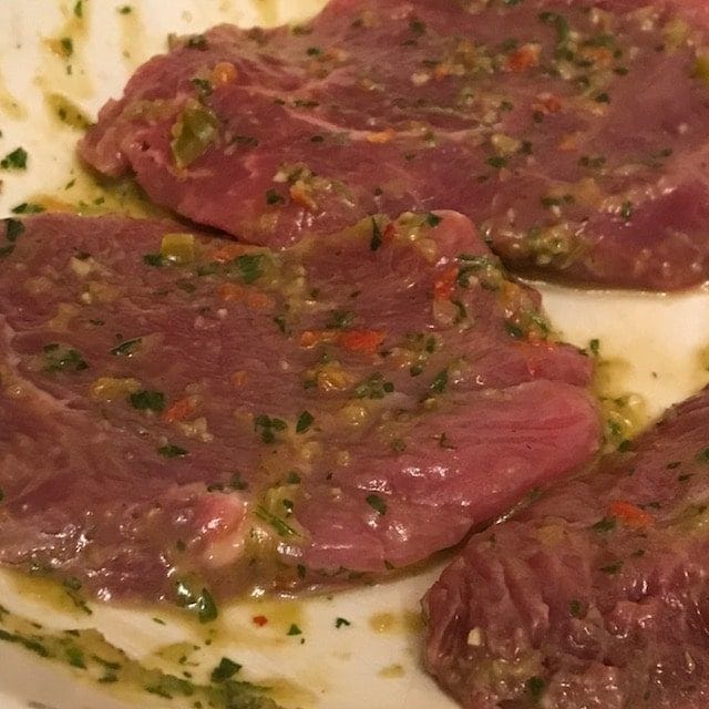 Raw meat steaks in a marinade on a plate.