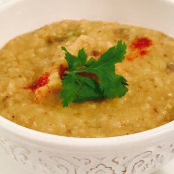 white bowl with yellow dal with coriander leaves and paprika garnish