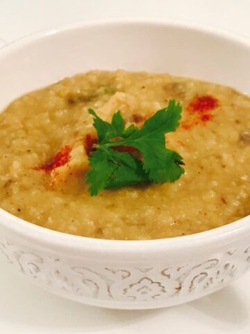 white bowl with yellow dal with coriander leaves and paprika garnish