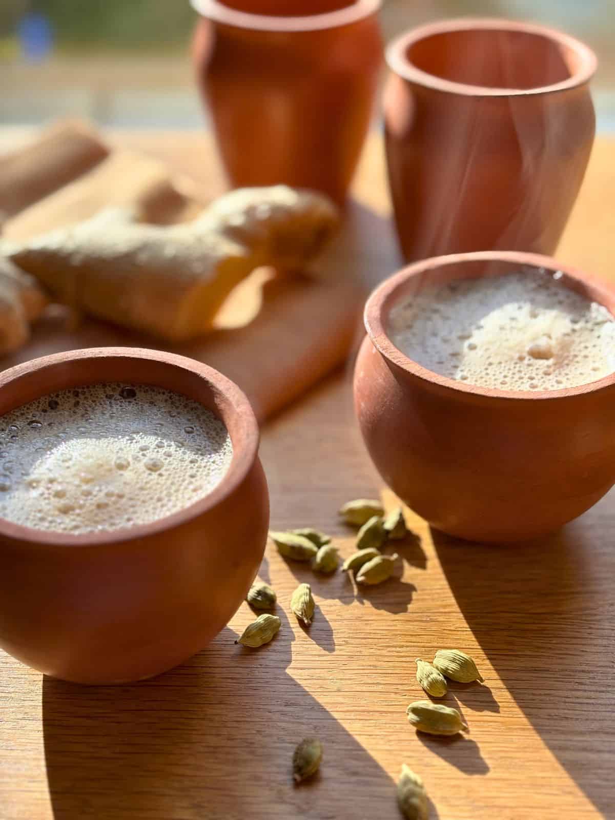 Two earthenware cups of masala chai near cardamom and fresh ginger.