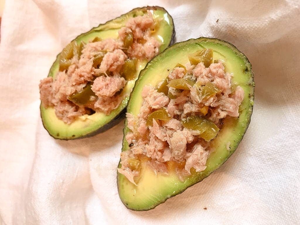 2 halves of avocado filled with tuna and jalapenos on white cloth