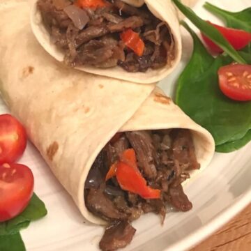 Two wraps showing pulled beef filling on plate with salad