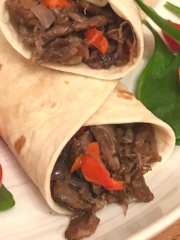 Two wraps showing pulled beef filling on plate with salad