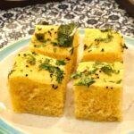 Image of four small squares of khaman dhokla with garnish on a plate.