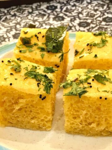 Image of four small squares of khaman dhokla with garnish on a plate.