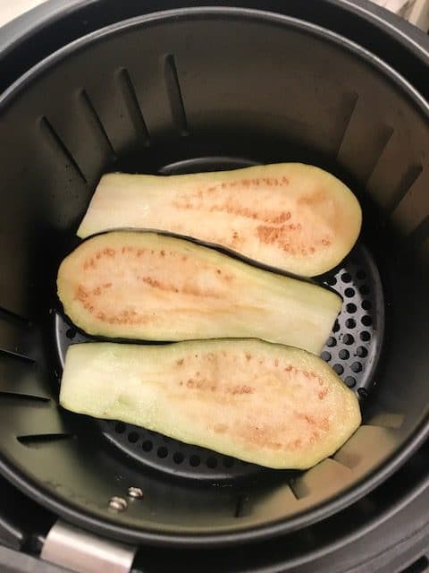 3 slices of raw eggplant lying flat, in the air fryer basket