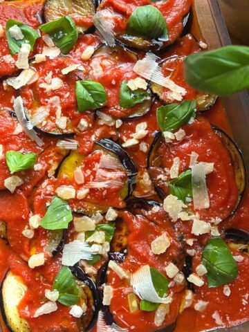 Close up of eggplant parmesan with basil in baking dish.
