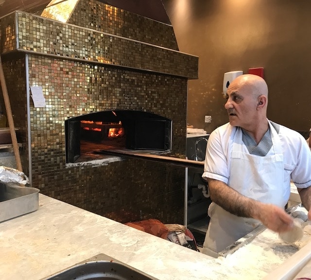 Baker preparing lahmacun in front of wood fired oven