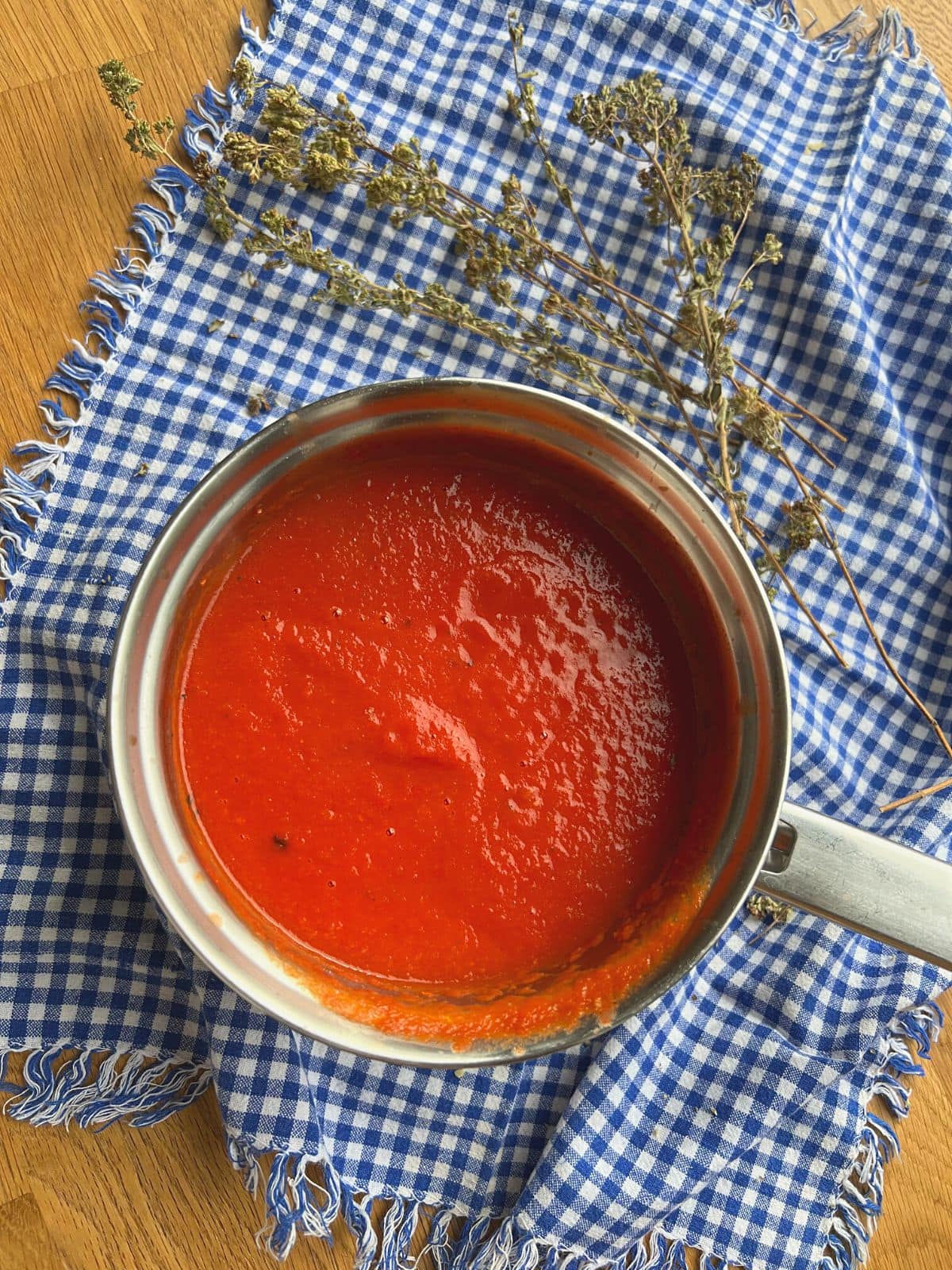 Tomato sauce in small pan alongside dried oregano.