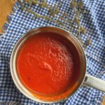 Tomato sauce in small saucepan with oregano sprigs.