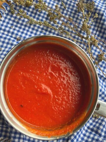 Tomato sauce in small saucepan with oregano sprigs.