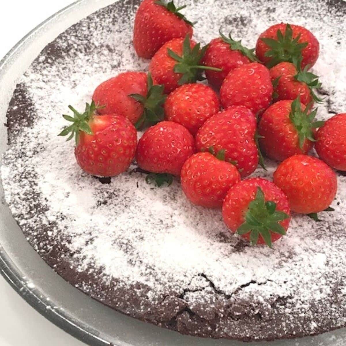 Kladdkaka on glass plate dusted with powdered sugar and whole strawberries