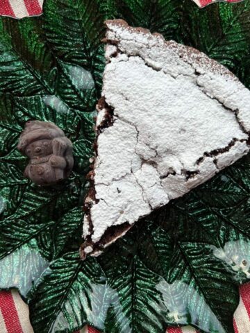 Slice of kladdkaka with powdered sugar on green Christmas plate.