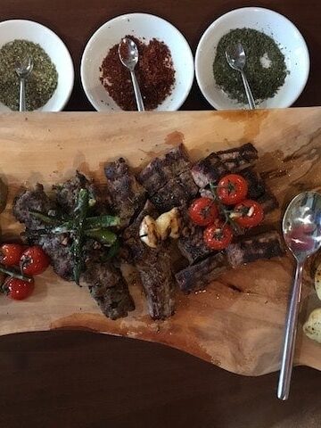 Lamb steak with vegetables on a wooden platter with bowls of dried herbs