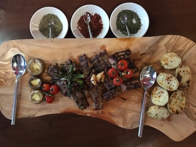 Lamb steak with vegetables on a wooden platter with bowls of dried herbs