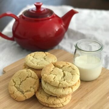 A pile of sugar cookies on a wooden board with a beaker of milk.