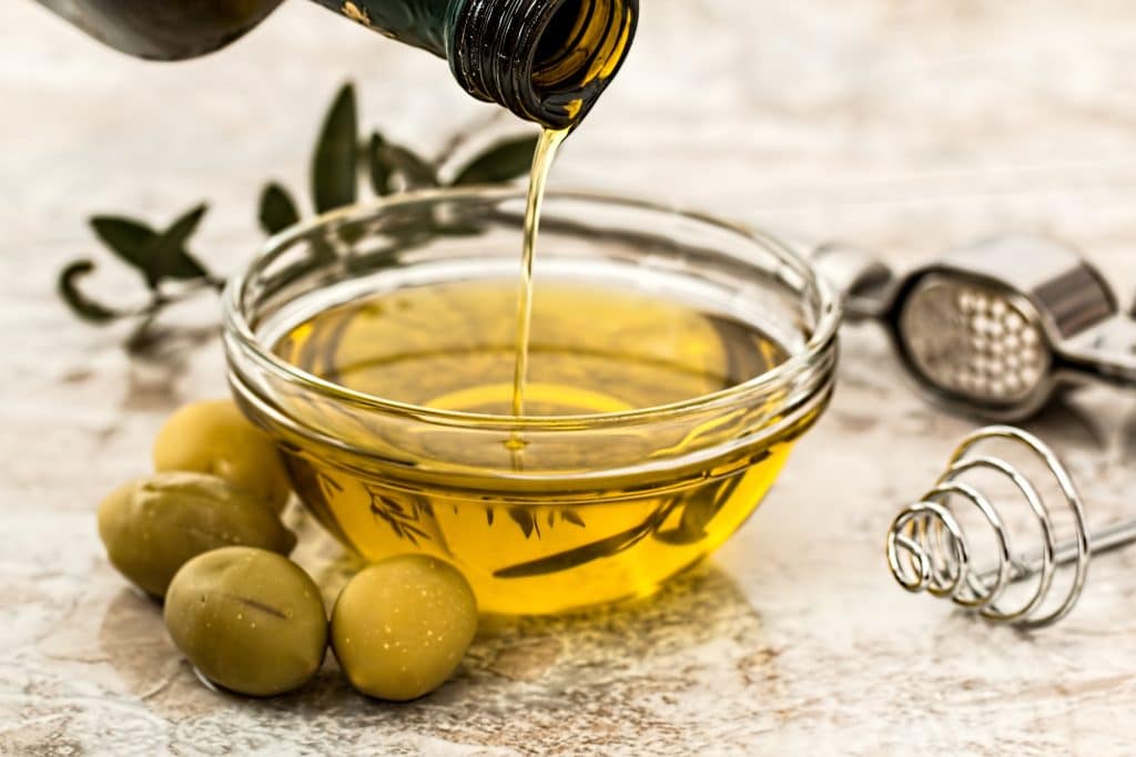 brown bottle pouring olive oil into a bowl next to some olives 