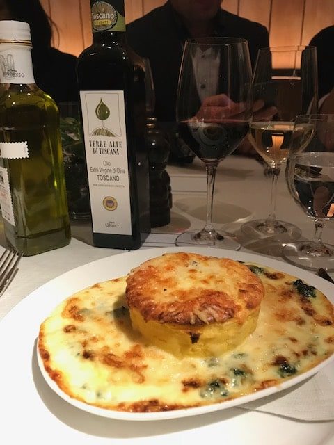 A dish of souffle with cheese and spinach next to a bottle of terre alto oil